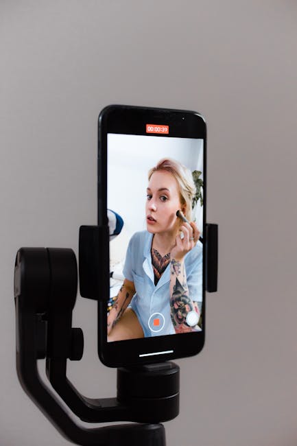 A woman records a makeup tutorial using a smartphone on a gimbal, capturing content for social media.